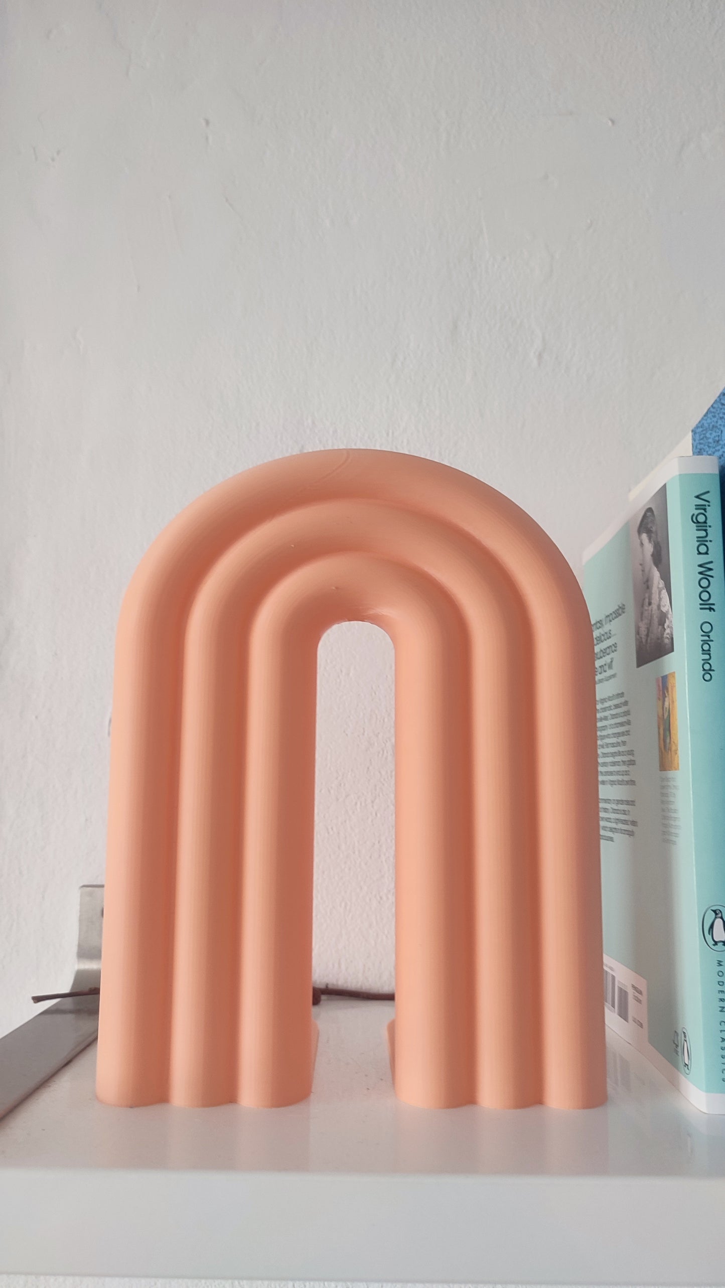Pink arch-shaped bookend on a surface with a blurred book in the background