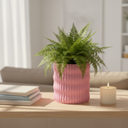 Pink Rivo ribbed planter with a lush green fern styled on a wooden table in a bright, modern living room with a stack of books and a lit candle